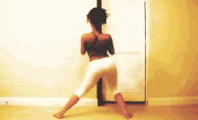 a woman in a black top and white pants is dancing in front of a wall .