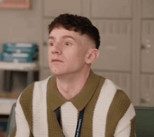 a young man wearing a striped sweater and a lanyard is sitting in a classroom .