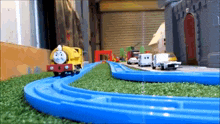 a toy train is going down a blue track on a grassy field .