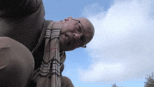 a bald man wearing glasses and a plaid scarf looks down at the sky .