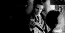 a man in a suit and tie is holding a microphone in front of a woman in a black and white photo .