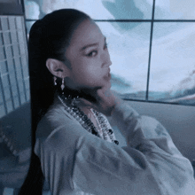 a woman with a ponytail and pearls around her neck looks at the camera