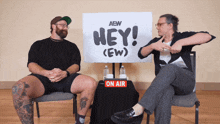 a man and a woman sit in front of a sign that says hey ( ew )