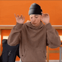a man wearing a brown hoodie and a black beanie is making a funny face