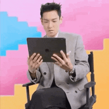 a man is sitting in a chair holding a tablet in his hands .