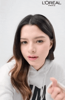 a woman wearing a white hoodie with l' oreal paris on the bottom