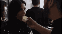 a man and a woman are kissing in a dark room while a woman wearing a mask looks on .
