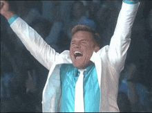 a man in a white jacket and blue shirt holds his arms up in the air