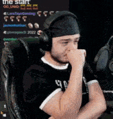 a man wearing headphones and a bandana is sitting in a chair with his hand on his face .