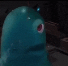 a blue toy with a red eye is sitting on a table in a dark room .