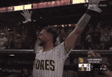 a man wearing a padres jersey holds his arms up in the air