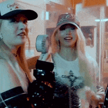 two women wearing hats are standing next to each other holding a small fan .