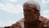 a man with a bandana on his head is drinking from a plastic bottle .