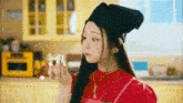 a woman wearing a red apron and a black beanie is eating a piece of food