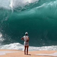a woman stands on a beach looking at a wave