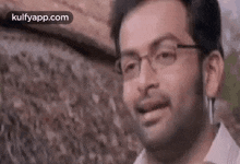 a man wearing glasses is smiling while standing in front of a wall .
