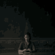 a woman sits at a table with her hands folded in front of a painting