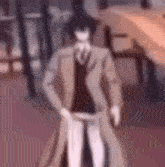a man in a trench coat and tie is standing in a room with his hands in his pockets .