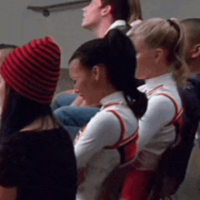 a group of cheerleaders are sitting in a row with one wearing a striped hat