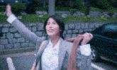 a woman in a suit is standing in front of a car with her arms outstretched .