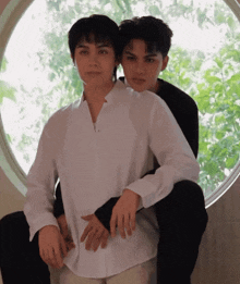 a man sitting on another man 's lap in front of a circular window