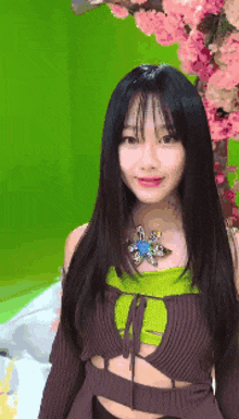 a woman with long black hair is standing in front of a green screen with pink flowers in the background .