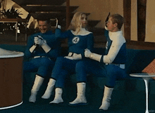 three people in fantastic four costumes are sitting on a couch in a living room .