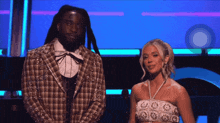 a man in a plaid jacket stands next to a woman in a white crop top