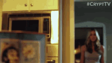 a woman is standing in a kitchen next to a microwave and a door .