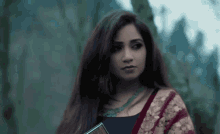 a woman in a saree is holding a book in her hand and looking at the camera .
