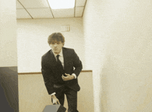 a man in a suit and tie stands in a hallway with an exit sign on the wall behind him