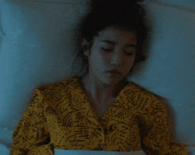a woman laying in bed wearing a yellow shirt that says ' mango ' on the front