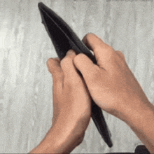 a person is holding an empty black wallet with their hands .