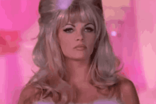 a woman with blonde hair and a pink background is wearing a wig .