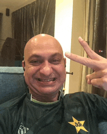 a bald man wearing a black shirt with a yellow star on it is giving a peace sign