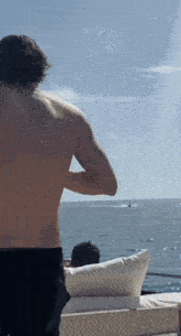 a shirtless man is standing on a boat in the ocean looking at a boat .