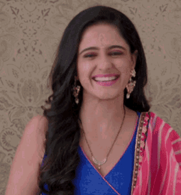 a woman wearing a blue top and a necklace smiles