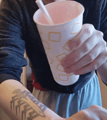 a person with a tattoo on their arm holds a cup with a straw in it