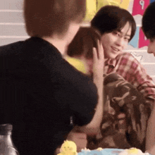 a group of people are sitting around a table and one of them is touching the face of another person .