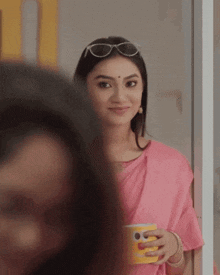 a woman wearing sunglasses and a pink saree is holding a cup of coffee .