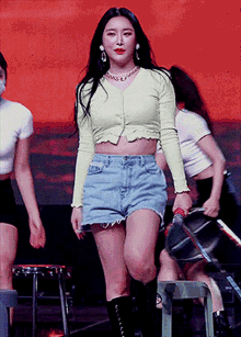 a woman wearing a green crop top and denim shorts is standing on a stage