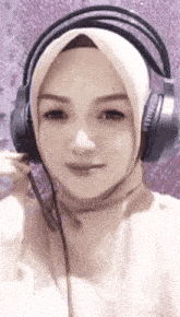 a woman wearing a hijab and headphones is smiling for the camera .