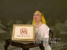 a woman with yellow hair is sitting at a table holding a framed picture with a m on it