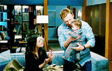 a man is holding a baby in his arms while a woman looks on .
