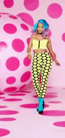 a woman with blue hair and yellow polka dot pants is dancing in front of a pink polka dot background