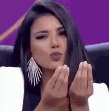 a woman with long black hair is blowing a kiss with her hands .
