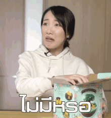 a woman in a white hoodie is holding a box that says ' ohsha ' on it