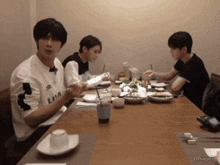 three young men are sitting at a table with one wearing a shirt that says lmr