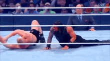 roman reigns is laying on the ground during a wrestling match while a referee looks on .