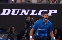 a man in a blue shirt is standing in front of a dunlop banner